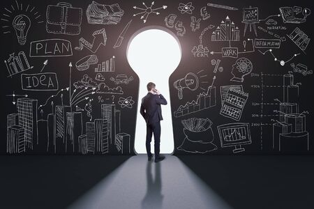 Rear view of a businessman against black wall with a keyhole pathの写真素材