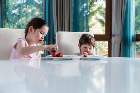 Cute children eating fresh ripe strawberries at homeの写真素材