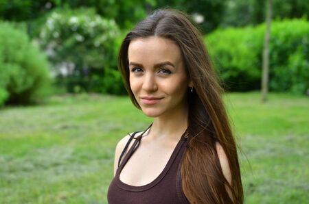 beautiful slender fairskinned girl smiling. It stands on a green background in nature. Fresh air. Summer.の写真素材