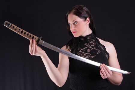 Young woman holding a samurai sword, katana, against blackの写真素材