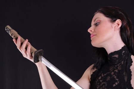 Young woman holding a samurai sword, katana, against blackの写真素材