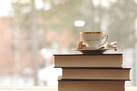 Porcelain cup with coffee on a stack of books by the windowの写真素材