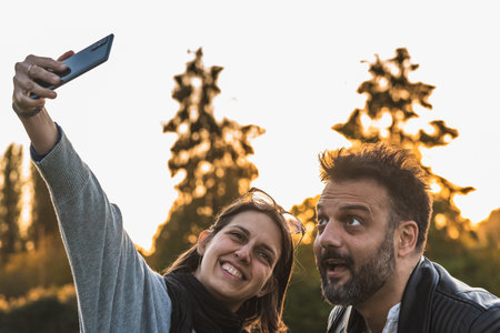 Couple taking selfie with funny faces outdoors in sunset sunlightの写真素材