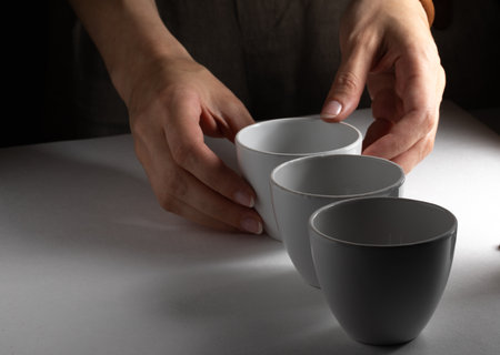 Person hand by three white cups in line on white table served with side natural lightningの写真素材
