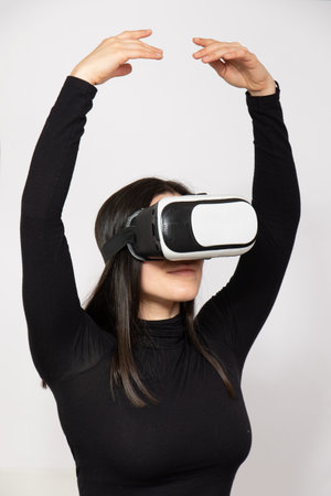 Pretty young caucasian woman isolated watch through VR white set with hands lifted up in white blank backgroundの写真素材