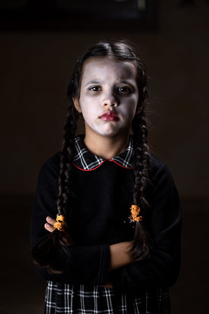 Portrait of little girl with Wednesday Addams costume during Halloween. Serious expression and dark...