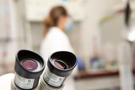 Ferrara, Italy, 8 Sept 2022: Closeup of the eyepieces of an optical microscope in focus and laboratory with a scientific researcher blurred in the backgroundの写真素材