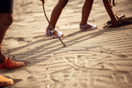 Detail of feet of children playing on the beach making drawings on the sand with a stick, concept of childhood, carefree and importance of play for kidsの写真素材