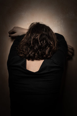 Lonely and abandoned woman who despairs with her forehead against the wall, turned away in a dark...