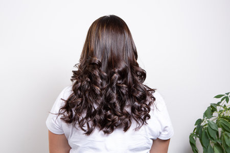 Half body portrait of rear view of a woman with long curly brown hair wear white t-shirt. High-quality photoの写真素材