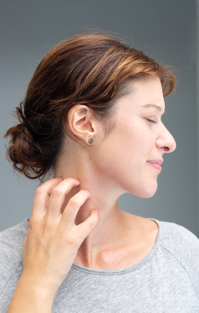 Caucasian girl scratching her neck due to an itchy allergic reactionの写真素材