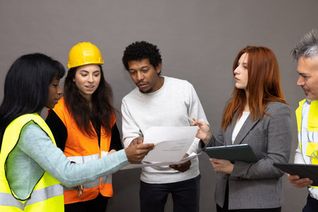 Mixed group of construction site workers watching and discussing the project. Males and females of...