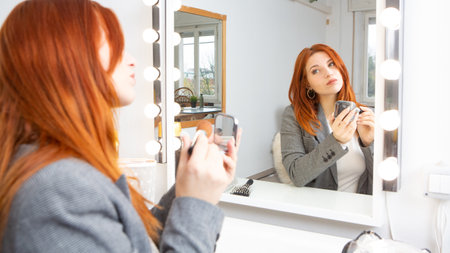 Businesswoman with elegant clothes doing her make up in front of the mirror before going to work. Female empowerment conceptの写真素材