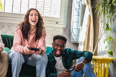 A young woman and man burst into laughter while engaged in a competitive video game session in a homely room bathed in natural lightの写真素材