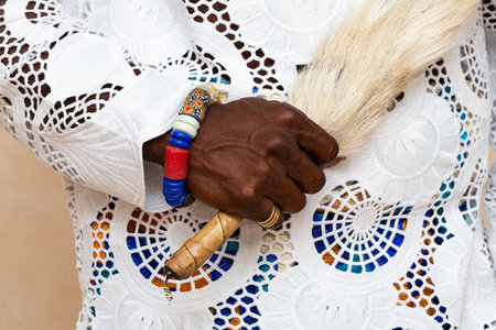 Close-up view of an African person's hand wearing traditional clothing, showing elaborate embroidery and holding an animal tail, complemented by vibrant beaded braceletsの写真素材