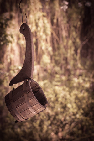 Old broken wooden ladle for russian bath hanging on a wire against a foliage background. Vintage lookの写真素材