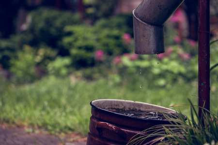 Large enamel tank full of water under a downpipe after a summer rain at country houseの写真素材