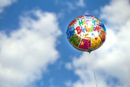 Colorful happy birthday balloon on a blue sky background in summertimeの写真素材