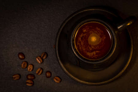 Black clay coffee cup with a saucer and scattered coffee beans near it on dark backgroundの写真素材