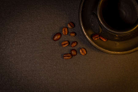 Black clay coffee cup with a saucer and scattered coffee beans near it on dark backgroundの写真素材