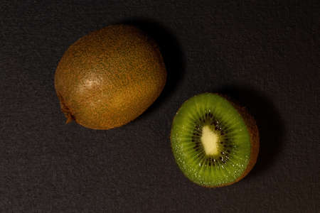 Kiwi fruits on black background. Whole kiwi and cut in half. Top view with copy space, flat lay.の写真素材