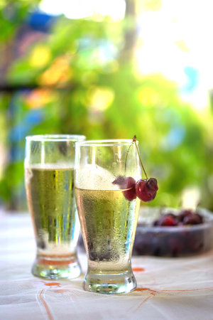 Refreshing, chilled summer beverage with water drops and cherries, set outdoors with a beautiful, bright green garden bokeh backgroundの写真素材