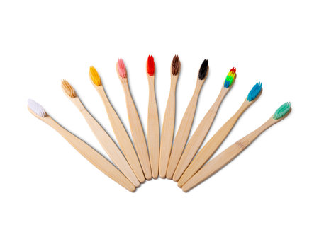 Nine natural bamboo toothbrushes with colorful bristles arranged in a fan shape, promoting sustainable dental hygiene, isolated on a white backgroundの写真素材