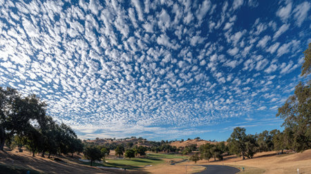Cloud-filled sky over a quiet golf course surrounded by tall oaks and rolling hillsの素材