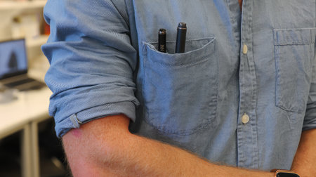 Rolled-up shirt sleeve with a pen clipped to the top pocket, suggesting work-in-progressの素材