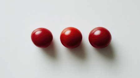 Minimalist shot of three cherry tomatoes placed symmetrically on clean whiteの素材