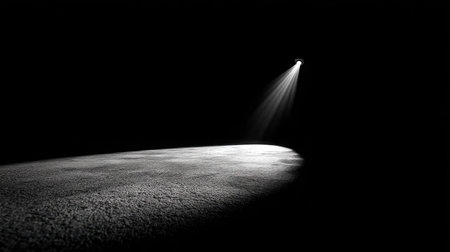 Single spotlight casting a focused beam of light onto a dark empty stage, dramatic shadow on floorの素材