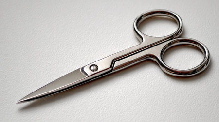 Small facial hair scissors opened slightly to show edge, resting on white surfaceの素材