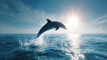A dolphin leaps gracefully out of the sparkling blue ocean under a clear sky, creating a perfect arc above the wavesの素材