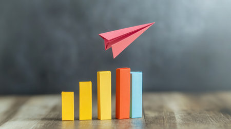 A paper airplane soaring above bar charts, representing innovative approaches to business growthの素材