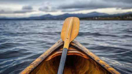 A captivating view of a kayak paddle resting in calm water, framed by mountains and dramatic clouds. This image embodies adventure and tranquility in nature.の素材