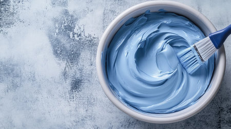 A bowl filled with smooth creamy blue paint, accompanied by a brush, captures the essence of creativity and artistic expression in home decoration and DIY projects.の素材