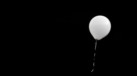 A striking image of a single white balloon floating in isolation against a solid black background, creating an elegant and serene atmosphere suitable for diverse artistic and event purposes.の素材