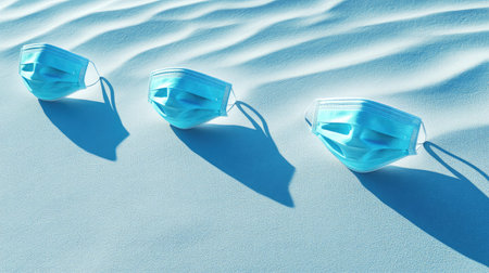 This image features three blue face masks discarded on soft sand, casting shadows in a serene environment. It symbolizes the aftermath of health regulations and their impact on society.の素材