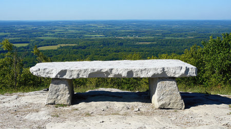 A serene stone bench placed at a scenic viewpoint, overlooking a vast green valley under a clear blue sky, perfect for relaxation and enjoying nature.の素材