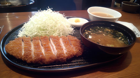 A delicious plate of crispy pork cutlet served with fresh cabbage, a side of soup, and dipping sauce, showcasing a flavorful dining experience.の素材