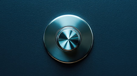 A closeup view of a sleek round metallic button situated on a dark textured surface, showcasing a modern design perfect for technology or user interface applications.の素材