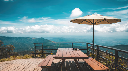 Enjoy a beautiful mountain view from a wooden table shaded by an umbrella, providing a serene spot to relax amidst nature's beauty under a bright blue sky.の素材