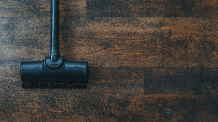 Close-up of a black vacuum cleaner head positioned on a polished wooden floor, highlighting the importance of cleanliness and home maintenance. Perfect for domestic imagery.の素材