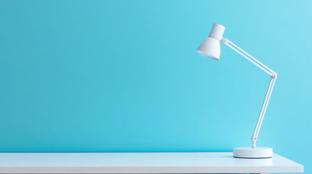 A stylish modern desk lamp emits warm light against a vibrant blue wall, creating an inviting workspace atmosphere. Ideal for enhancing interior decor in offices or study areas.の素材