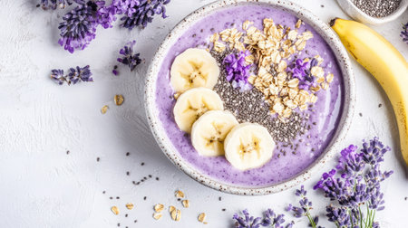 Purple smoothie bowl topped with granola, banana slices, and chia seeds on a white counterの素材