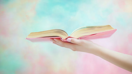 Delicate hand holding a book on a light background, pages slightly fanned openの素材