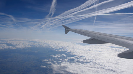 Contrails from another aircraft visible from airplane window against a vivid skyの素材