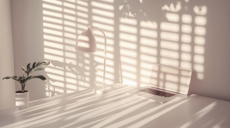 Bright and airy desk scene featuring a lamp and laptop on a white surface with shadows cast from a nearby windowの素材