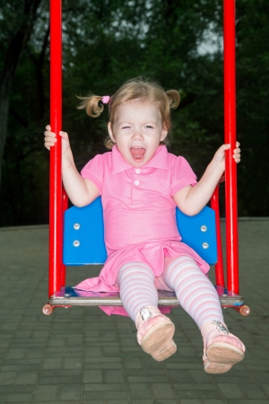 The little girl in pink dress shakes on swing in parkの写真素材
