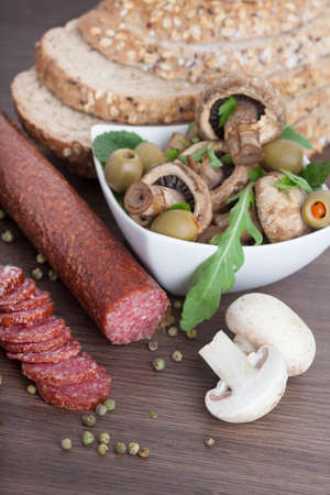 Salami sausage on a wooden table with mushrooms and olivesの写真素材